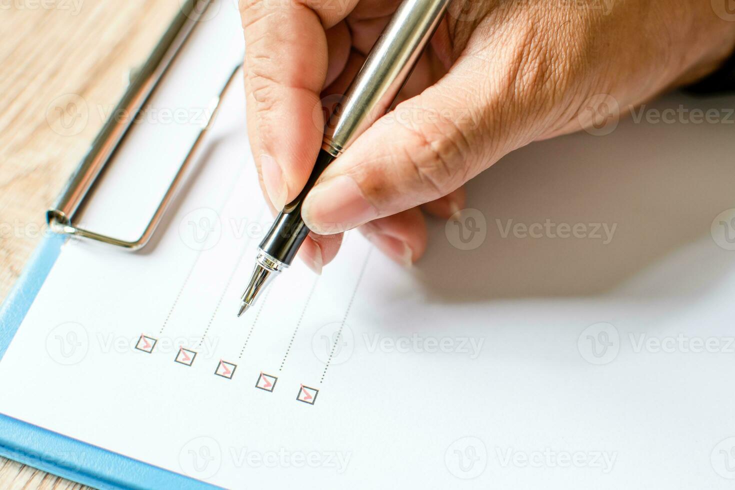 Close- up, Men's fingers holding pen writing on checklist paper and the format for filling in information in business concept. Businessman writing on checklist on wooden desk. Blurred wood background photo