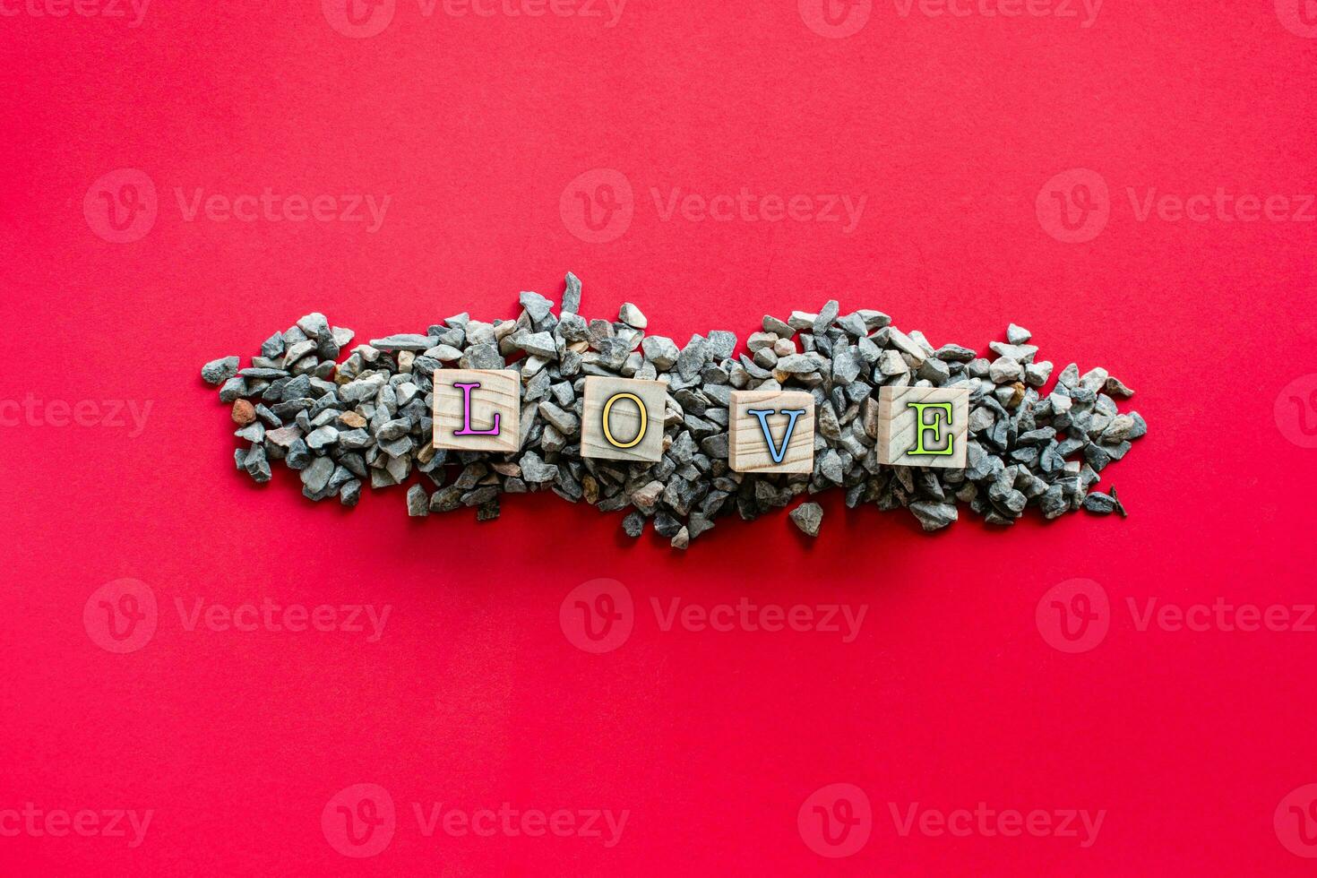 The letters LOVE in various colors on the wooden cube. Which is on a pile of small stones or pebbles. Concept of the day of love or Valentine's Day. Top view, Closeup, Copy space for design and text photo