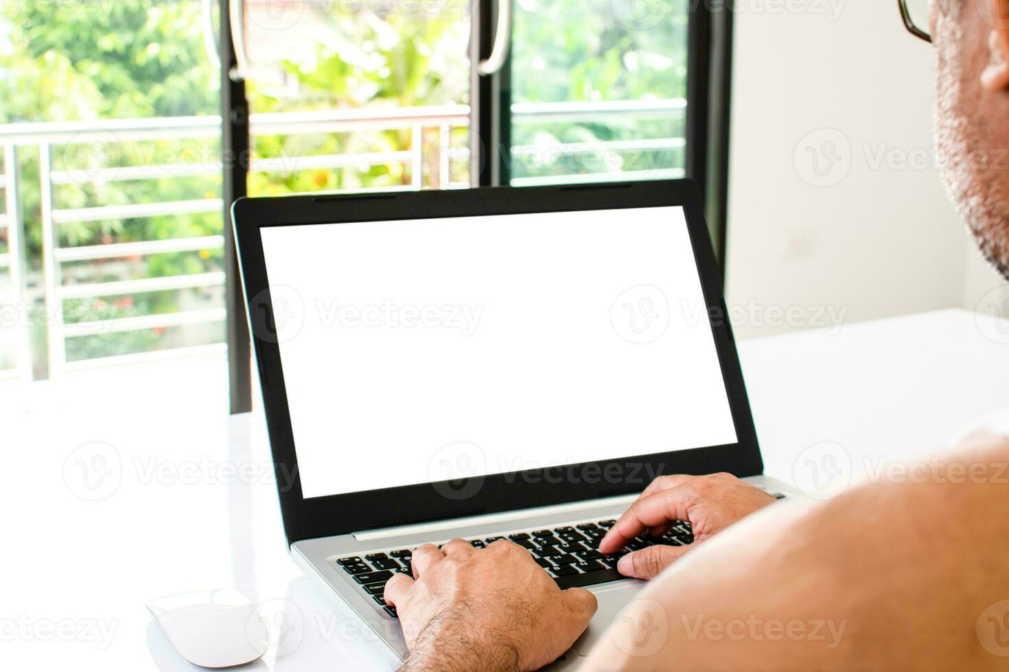 de cerca, personas trabajo hogar blogger un hombre se sienta y mecanografía un documento con un ordenador portátil en un blanco mesa en el vivo habitación a hogar. el blanco pantalla es blanco para diseño, texto, letra Bosquejo, recorte camino foto