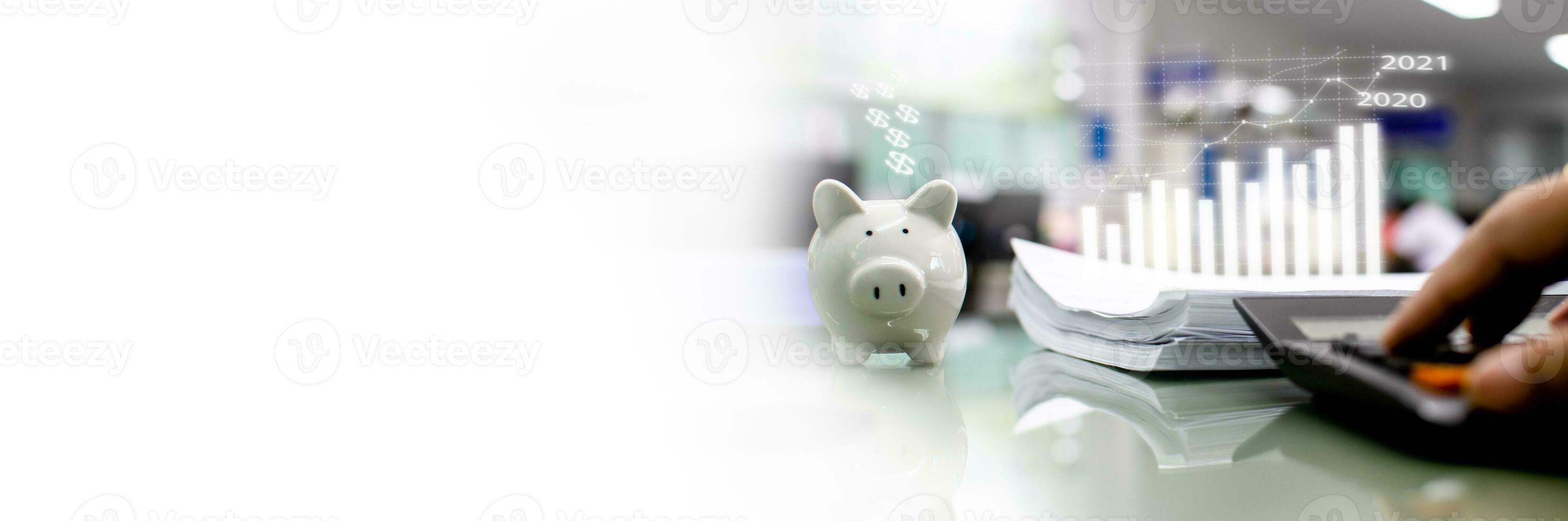 Closeup the white piggy bank, many papers, sheets on the glass desk. Concept a man's finger pressing a calculator on a glass table in bank office. Copyspace for design, text. White Blurred background photo