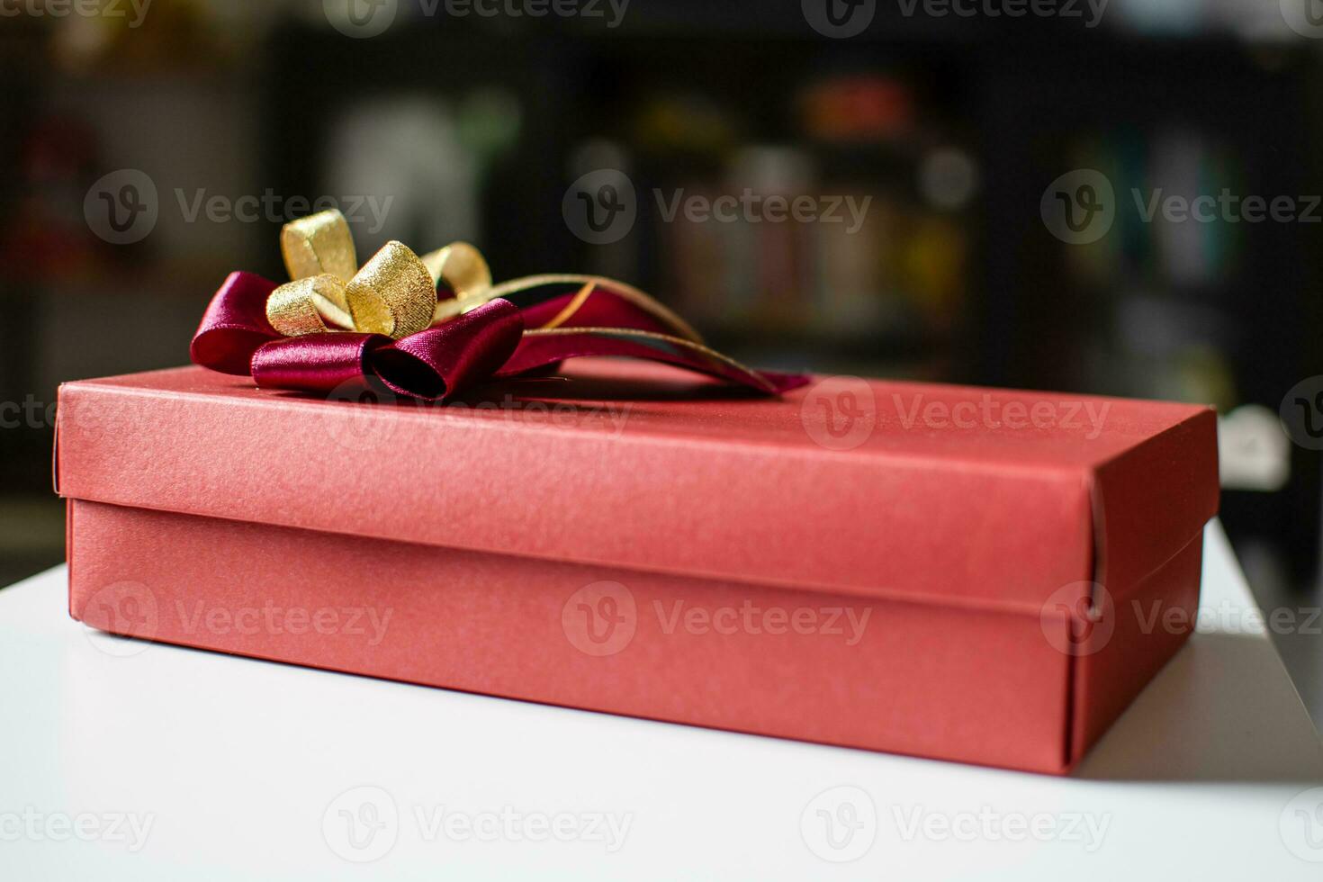 The red color Presents celebrate box with red and gold ribbons placed on a white table with copy space on the top can input text, take close-up photography, and top view, blurred background photo