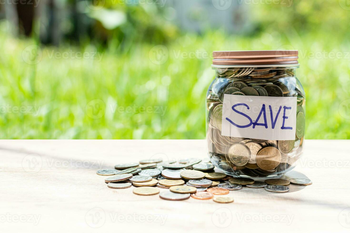 The coins and text SAVE in a glass jar placed on a wooden table. Copy space top and lelftl for content. Concept of saving money for investment and emergency situations. Close up, Blurred background photo