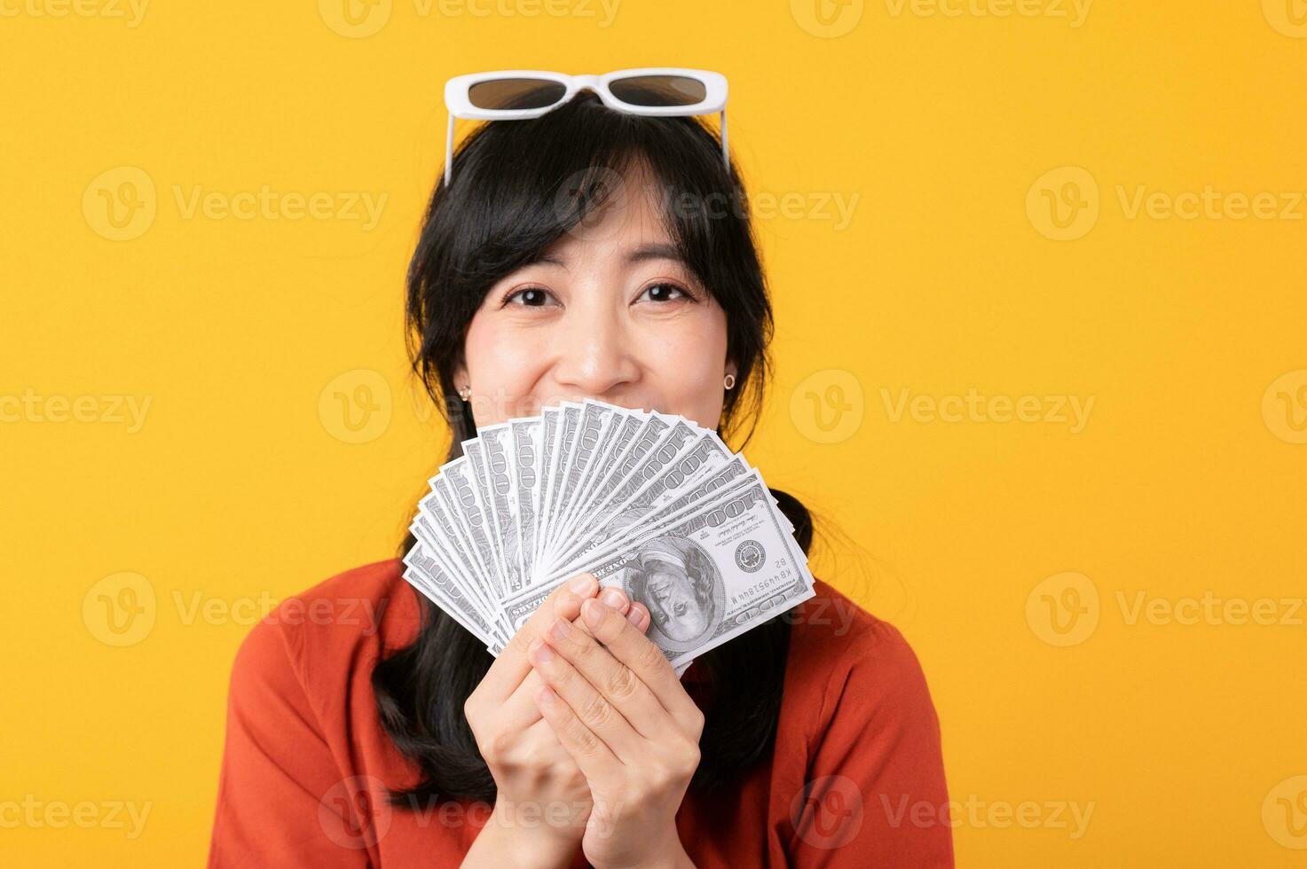 Portrait young beautiful asian woman happy smile dressed in orange clothes showing cash money isolated on yellow background. Pay and purchase shopping payment concept. photo