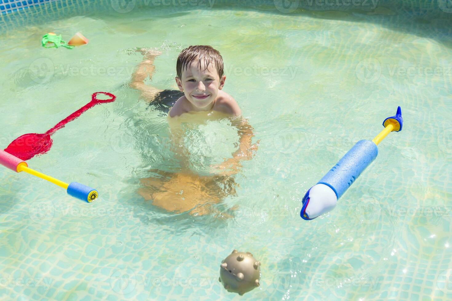 A child swims in the pool with toys. Boy bathes in water photo