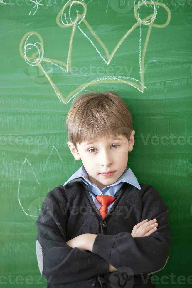 Funny child against the blackboard. Schoolboy boy with crown pattern photo