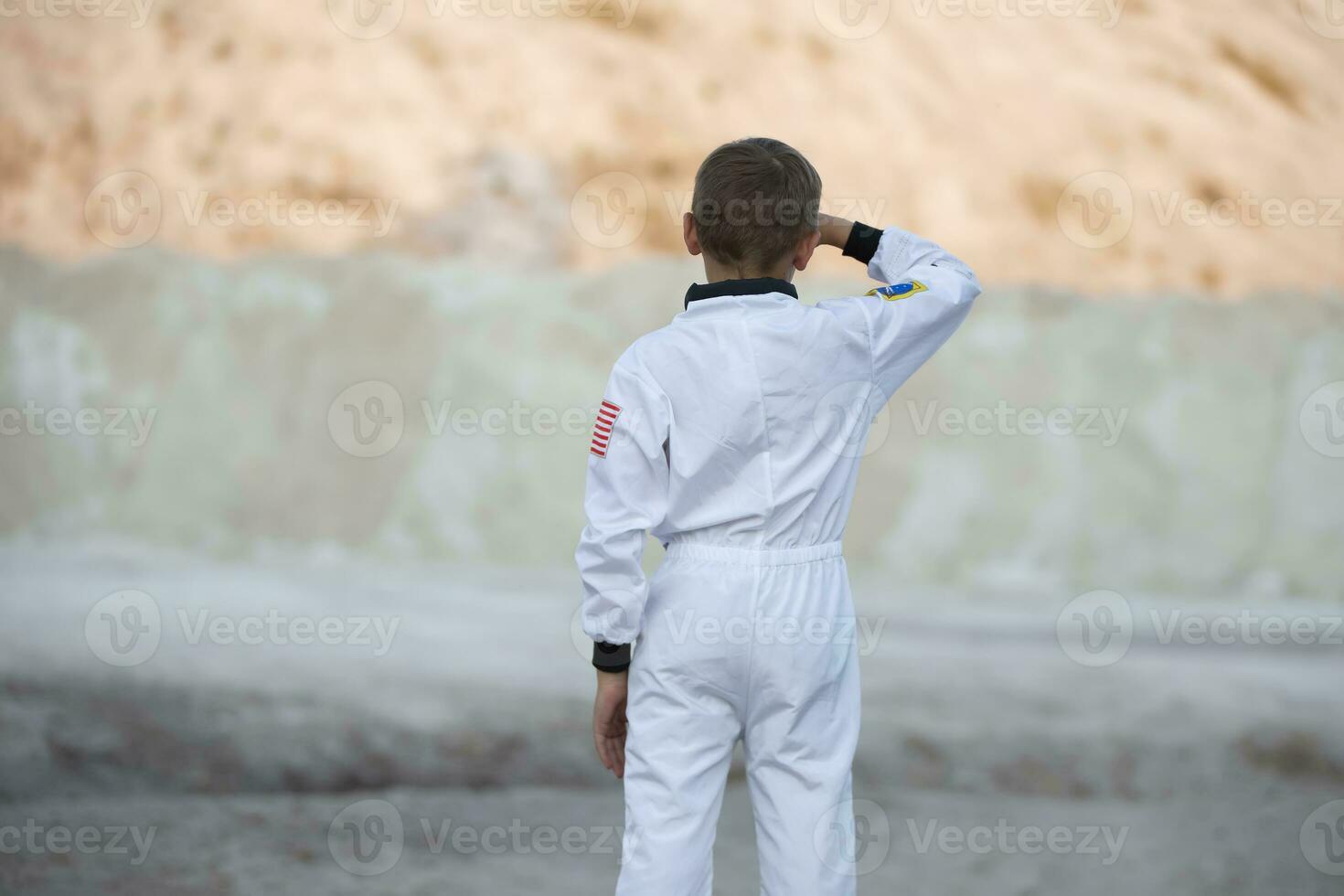 A young boy dressed as an astronaut looks at the exotic landscape of the white mountains. photo