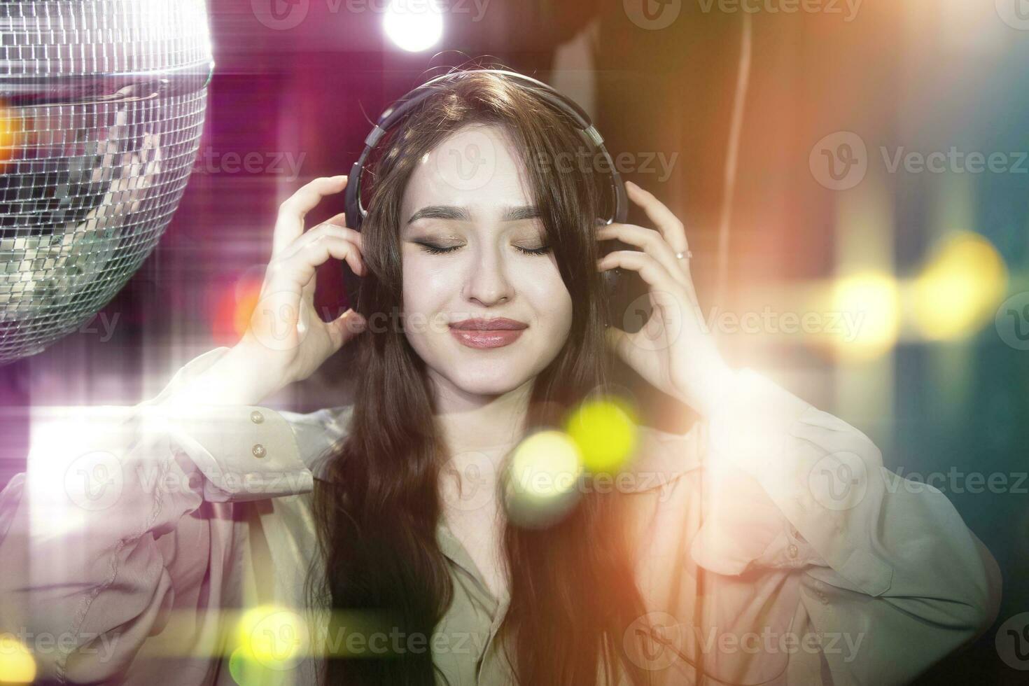 Beautiful fashionable girl in headphones enjoy listening to cool music on the bokeh background from the disco ball. photo