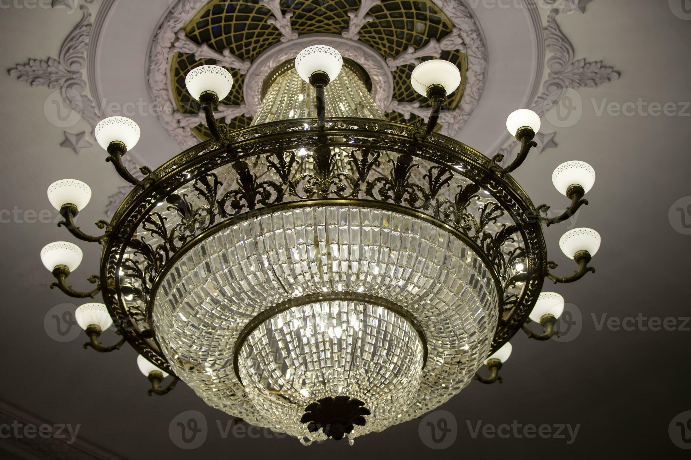 There is a beautiful theater chandelier on the ceiling and an expensive glass lamp. 32422709
