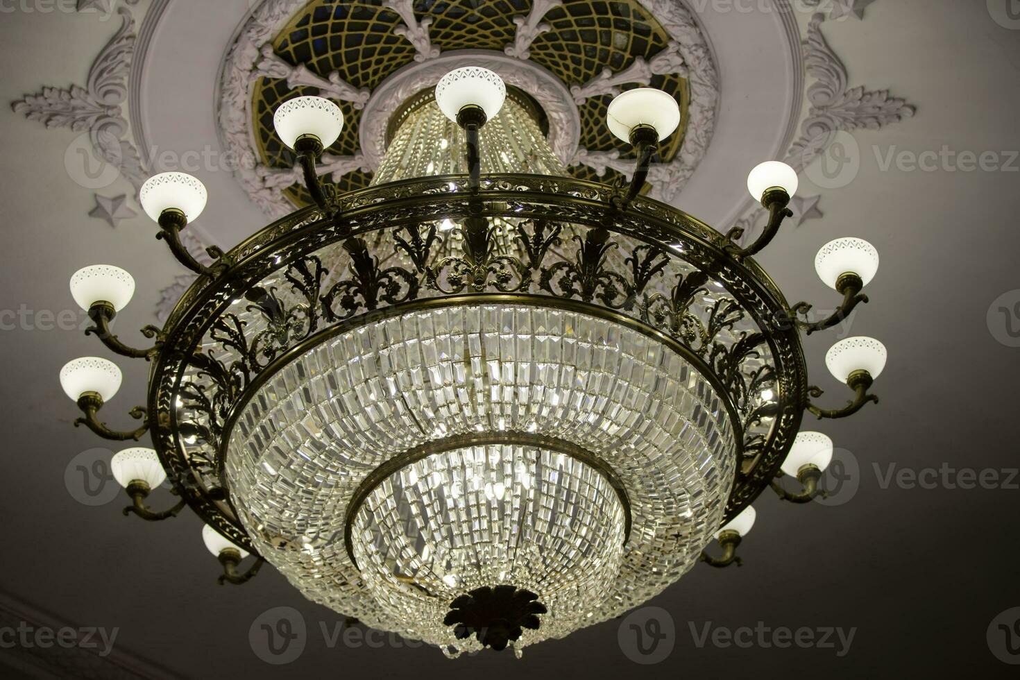 There is a beautiful theater chandelier on the ceiling and an expensive glass lamp. photo