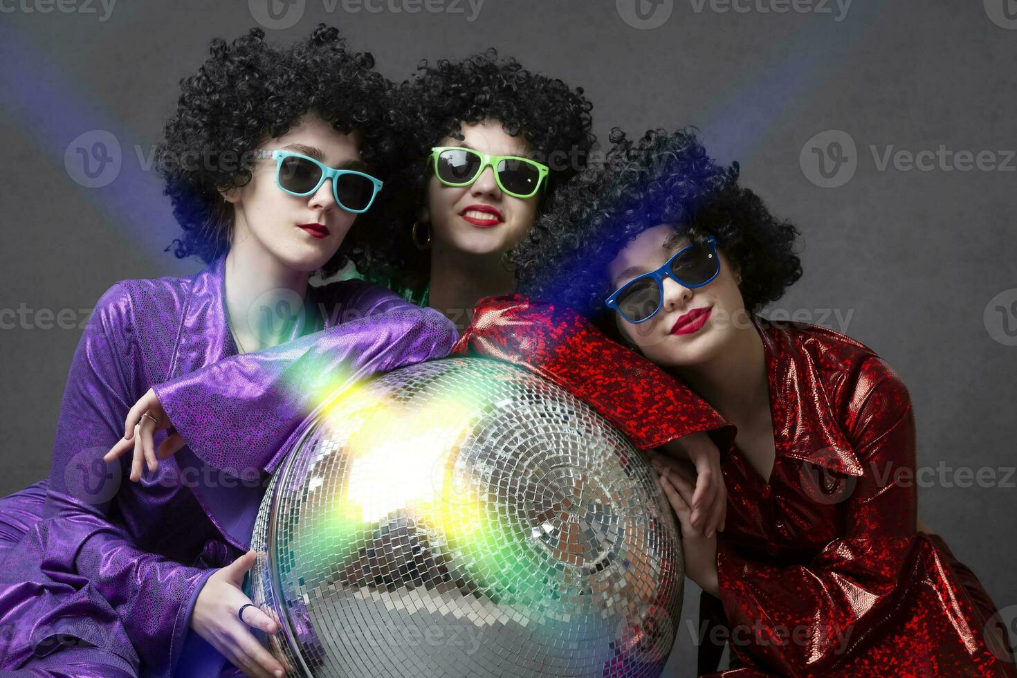 Music or dance group of girls in disco style posing on a gray background with a disco ball. The dance era of the eighties and late seventies. photo