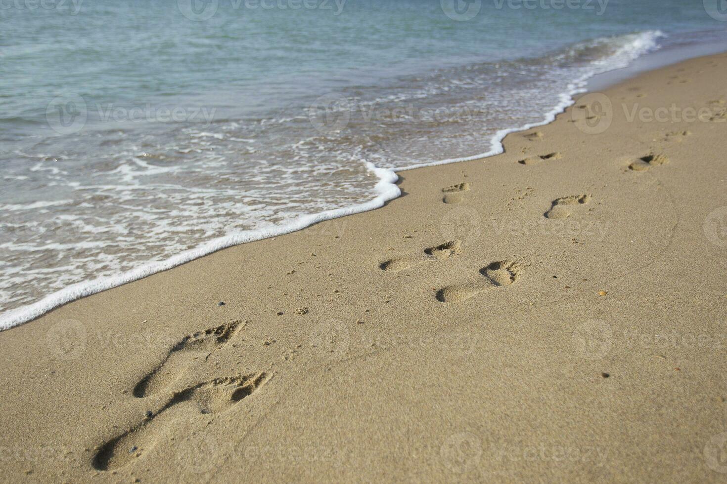 Footprints in the sand against a sea wave photo