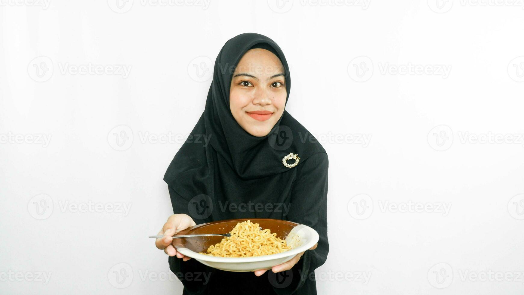 Young asian woman isolated on white background holding a plate of noodles with fork and eating it photo