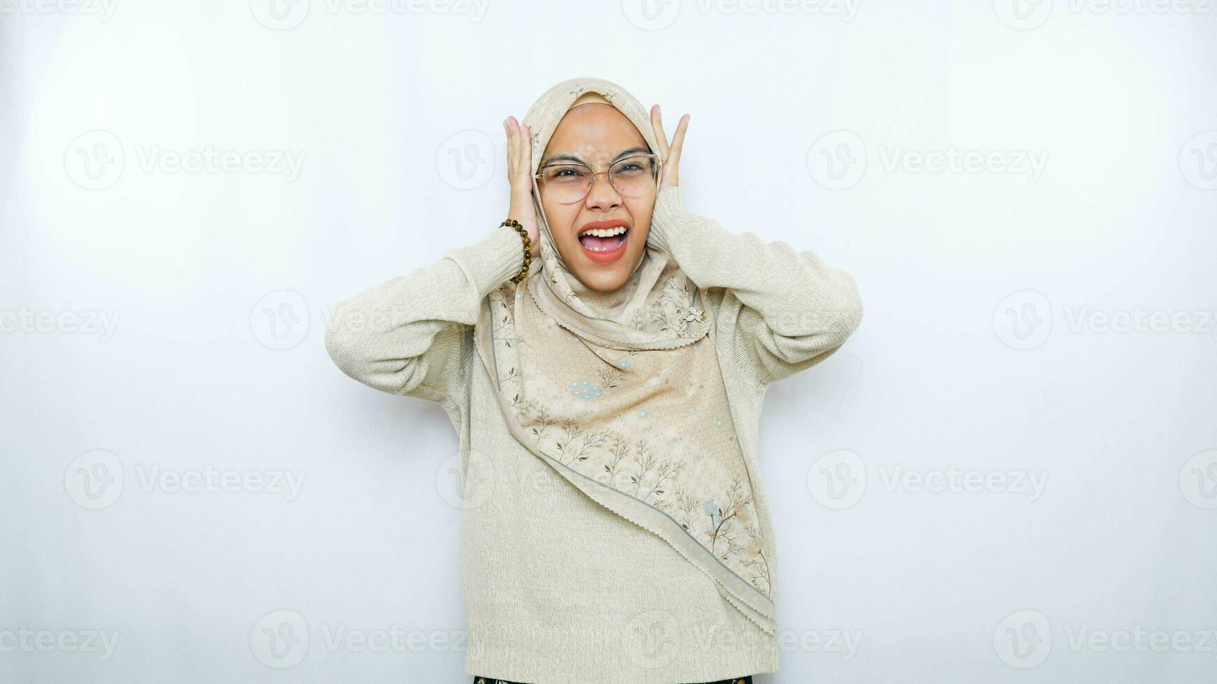 Young beautiful Asian Muslim woman wearing a headscarf shouting and screaming loud with a hand on her mouth. communication concept. photo