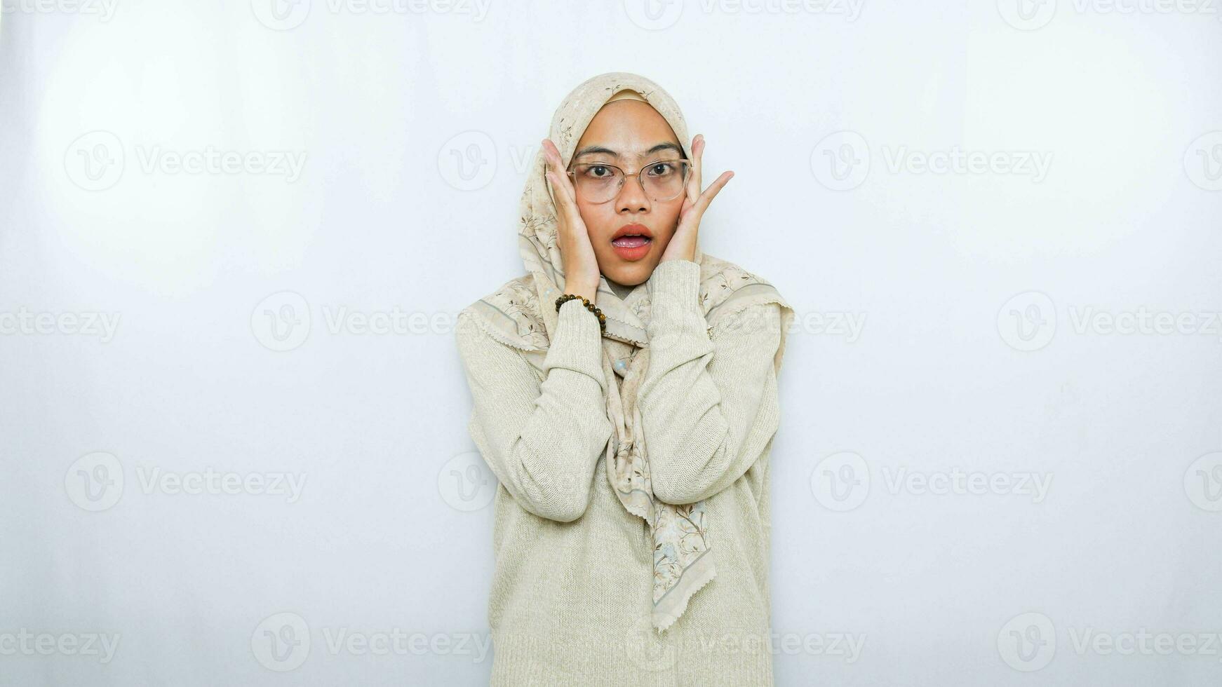 Young beautiful Asian Muslim woman wearing a headscarf shouting and screaming loud with a hand on her mouth. communication concept. photo
