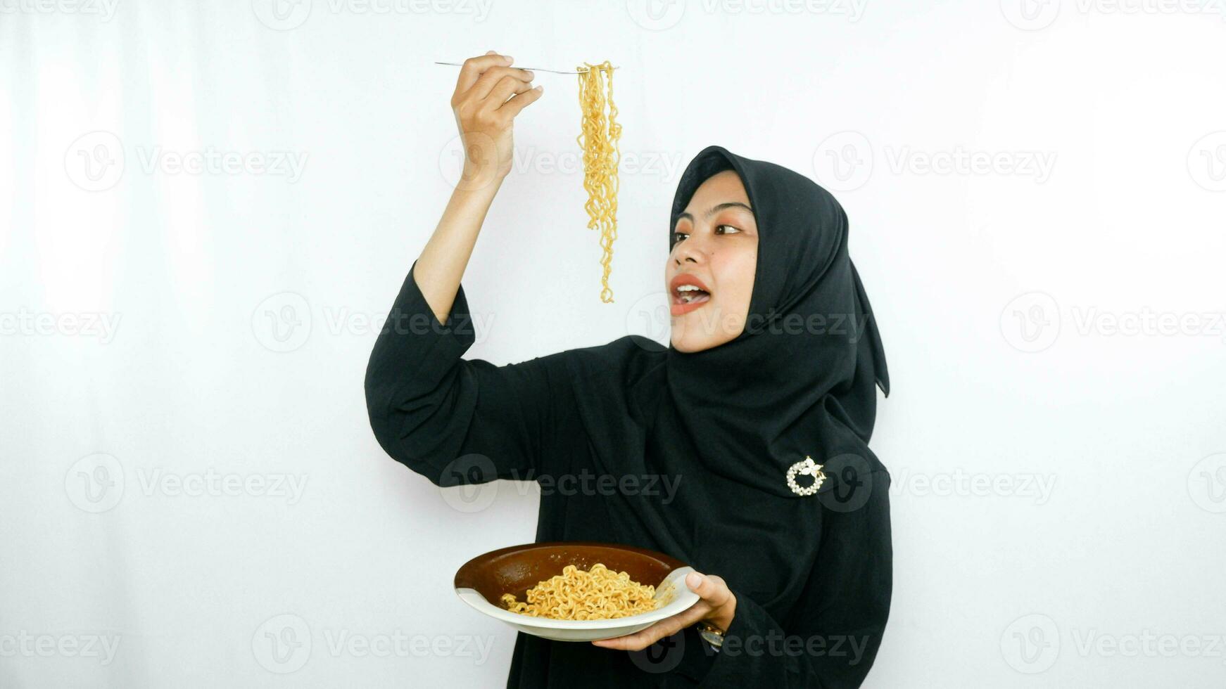 Young asian woman isolated on white background holding a plate of noodles with fork and eating it photo