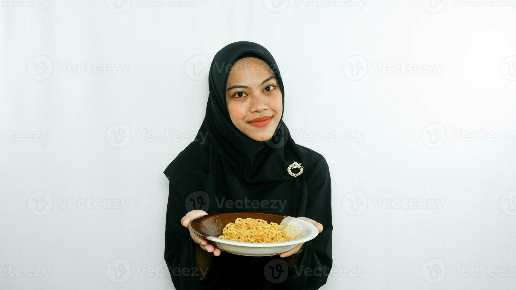 Young asian woman isolated on white background holding a plate of noodles with fork and eating it photo