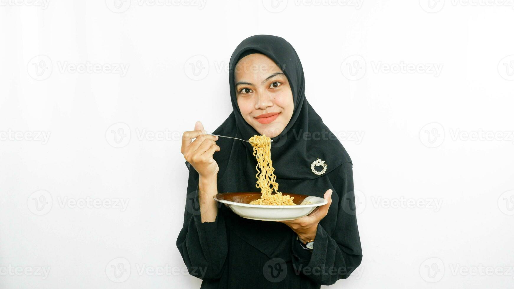 Young asian woman isolated on white background holding a plate of noodles with fork and eating it photo