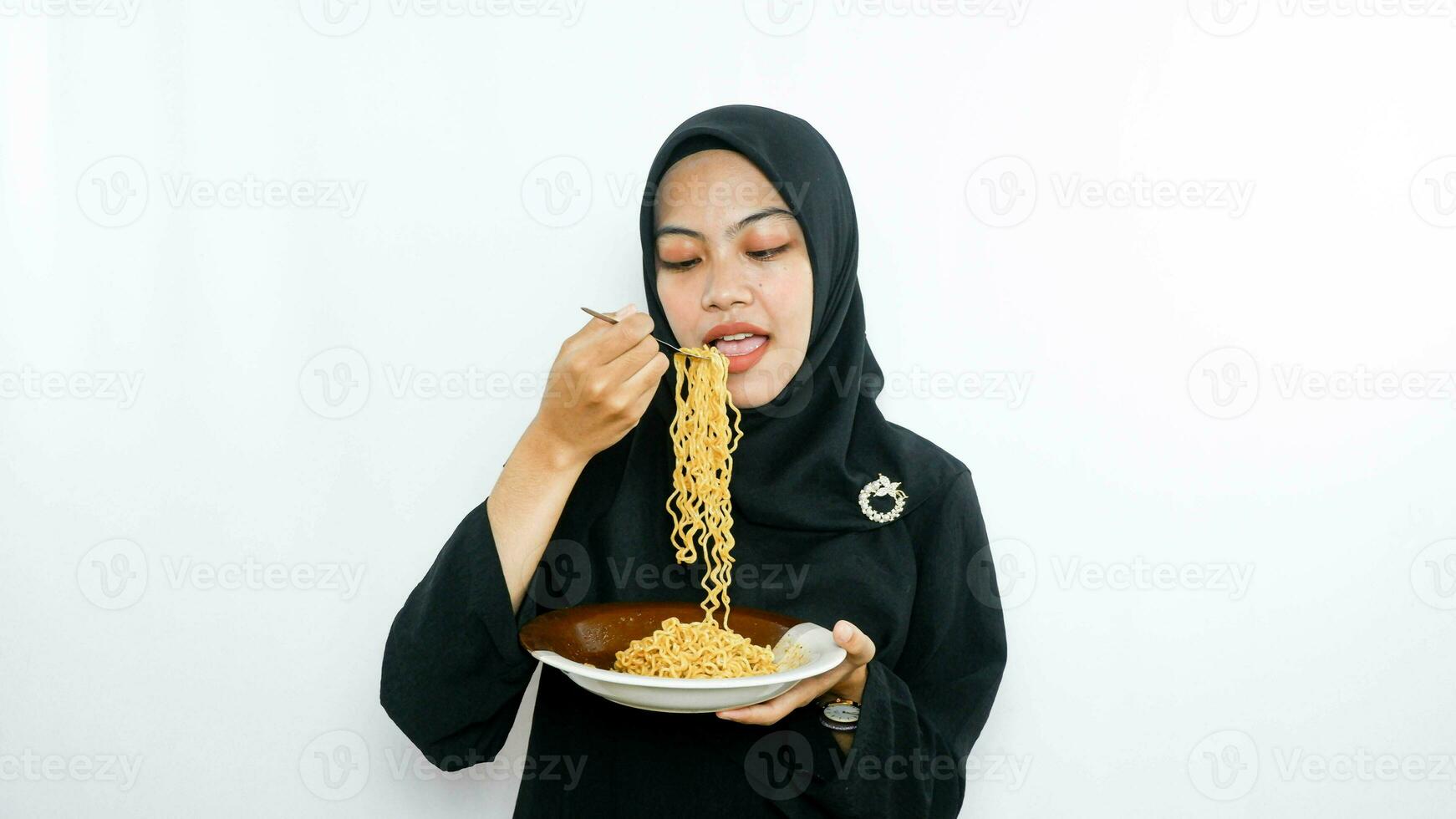 Young asian woman isolated on white background holding a plate of noodles with fork and eating it photo