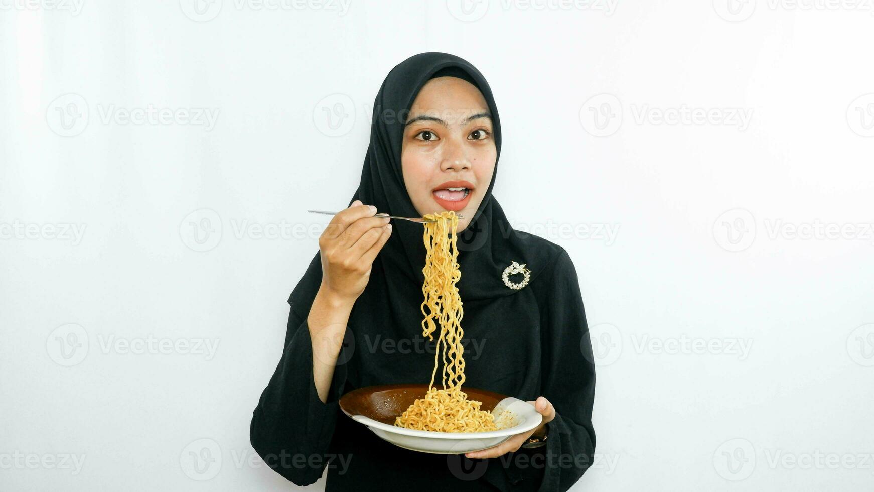 Young asian woman isolated on white background holding a plate of noodles with fork and eating it photo