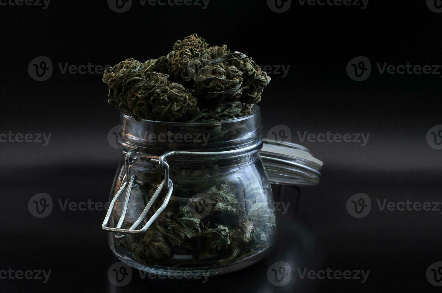 noir still life with glass mason jar full of dry medical cannabis buds on black background photo