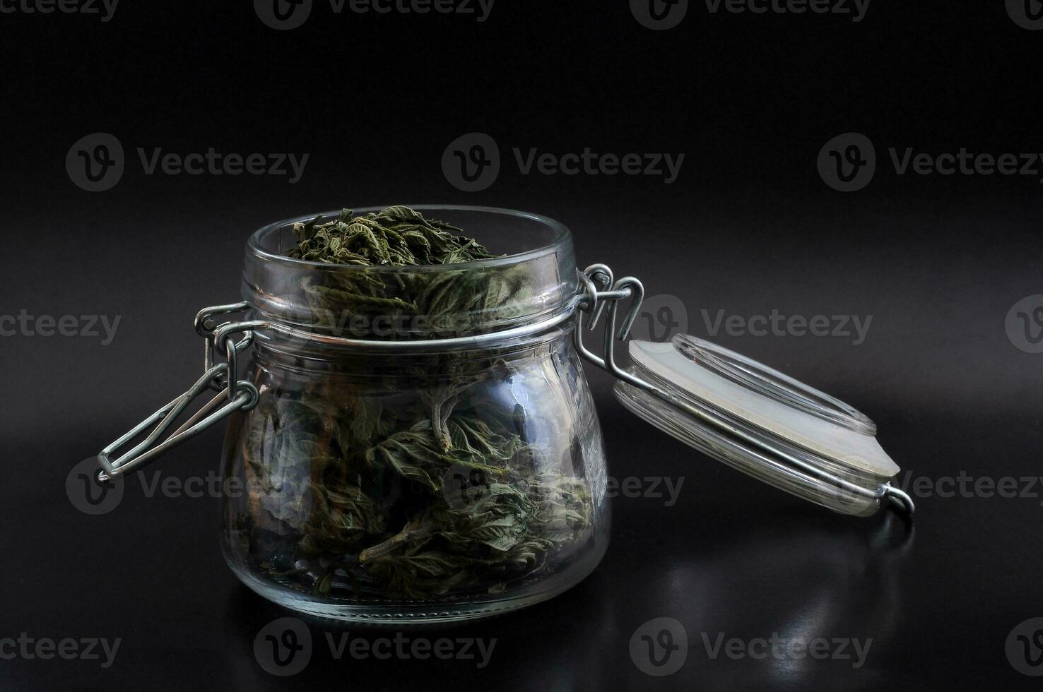 noir still life with glass mason jar full of dry medical cannabis buds on black background photo