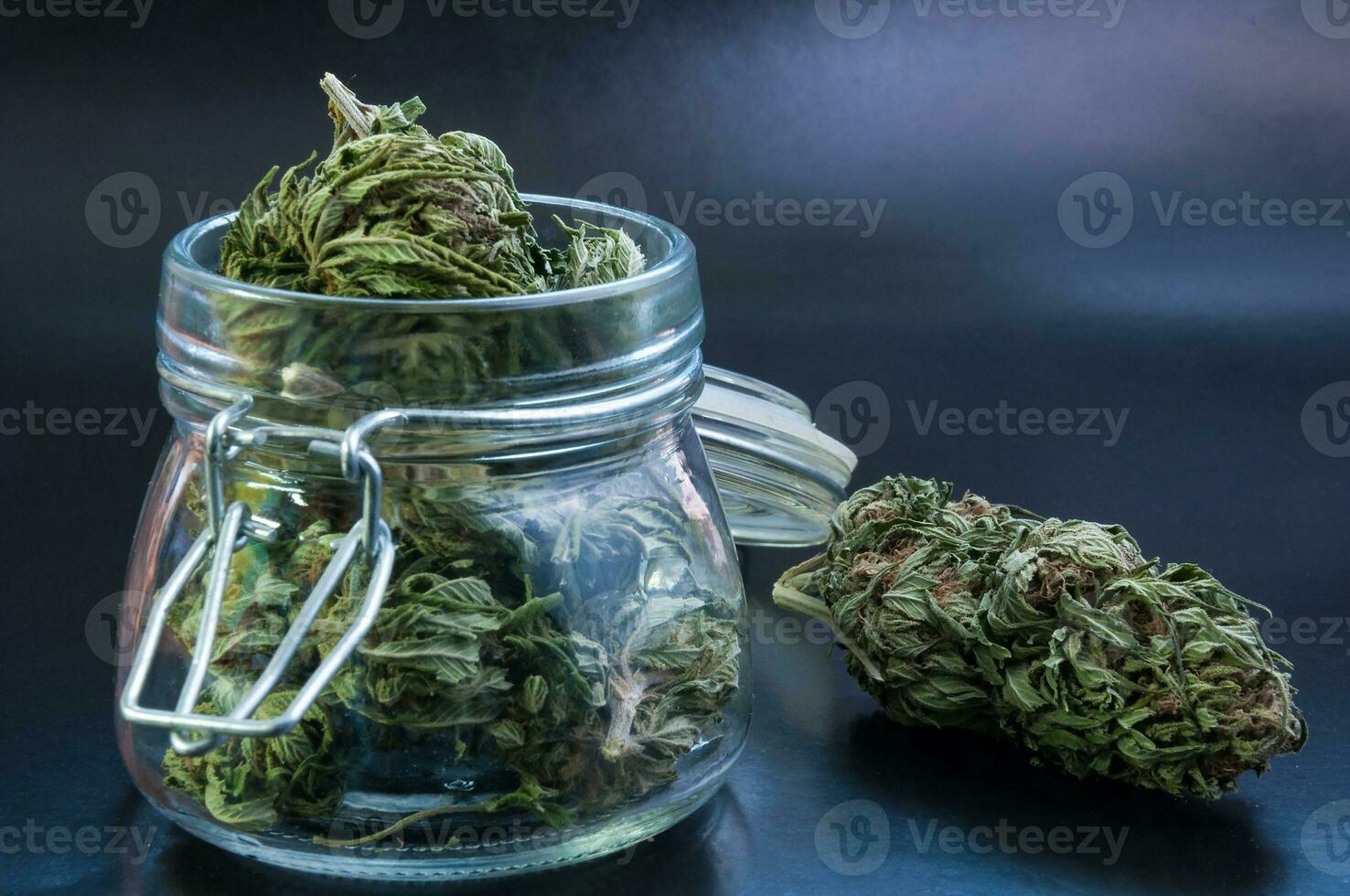 noir still life with glass mason jar full of dry medical cannabis buds on black background photo