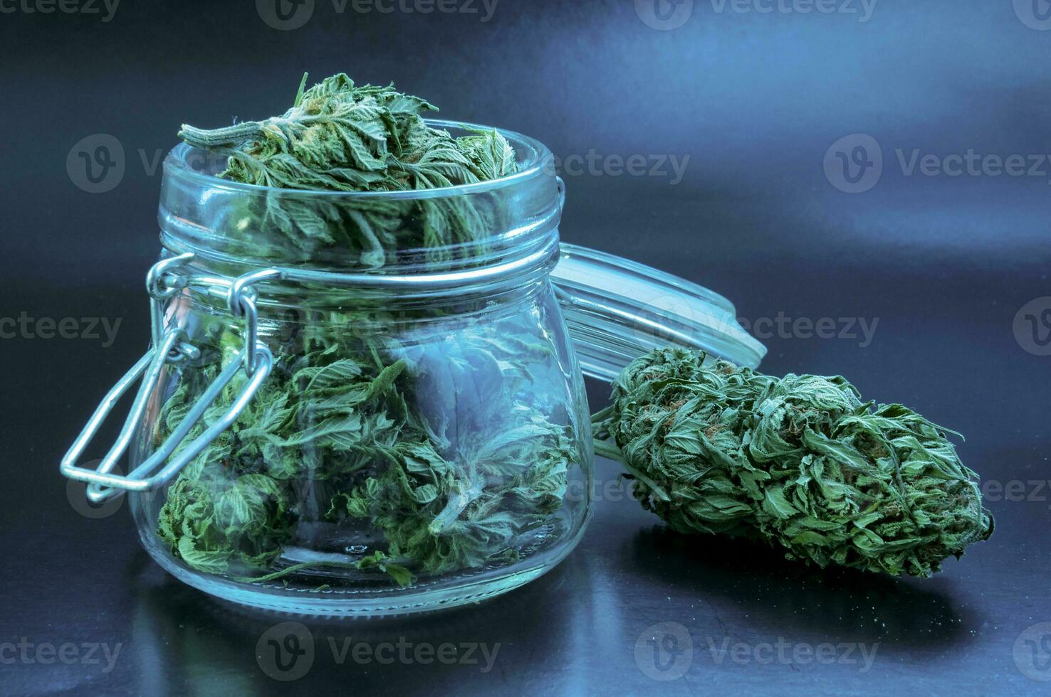 noir still life with glass mason jar full of dry medical cannabis buds on black background photo