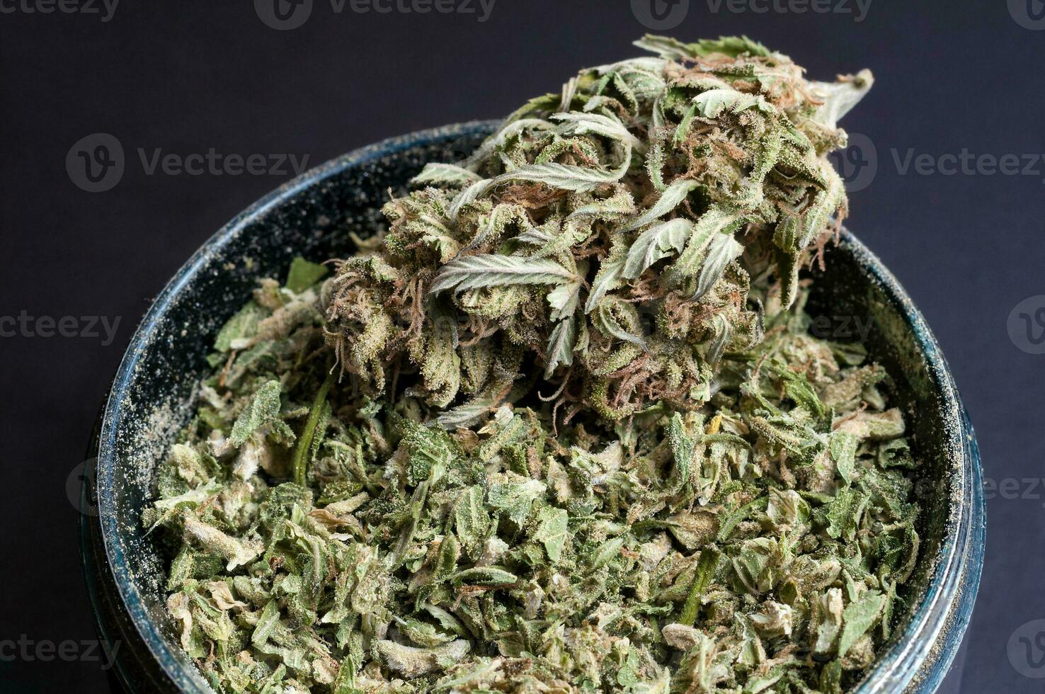 dry flowers of medical marijuana and grinder full of crushed buds close up on black background photo