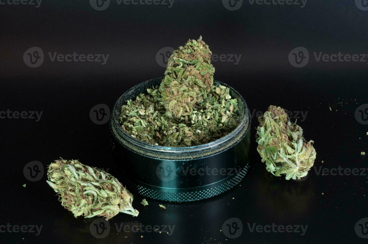 dry flowers of medical marijuana and grinder full of crushed buds close up on black background photo