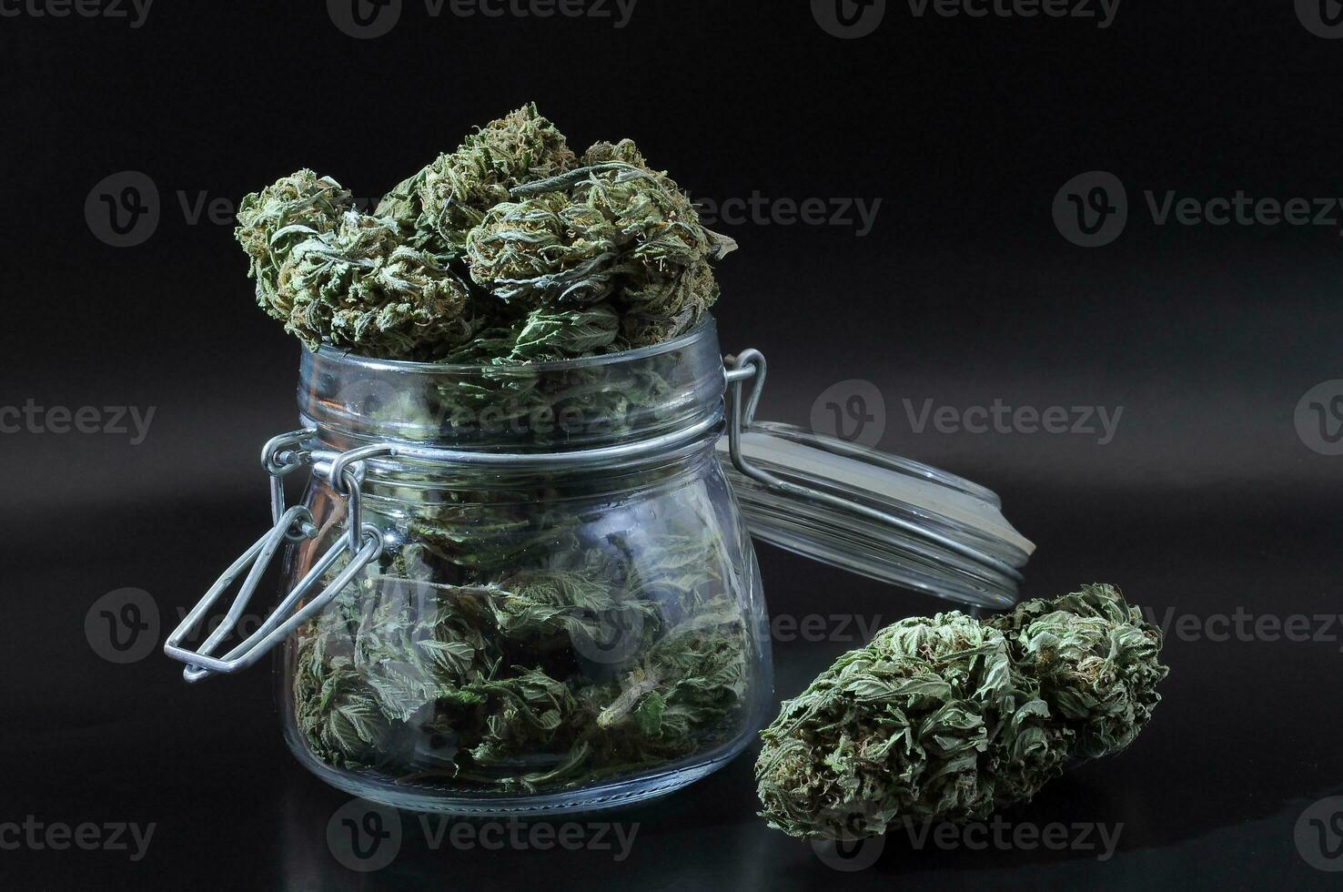 noir still life with glass mason jar full of dry medical cannabis buds on black background photo