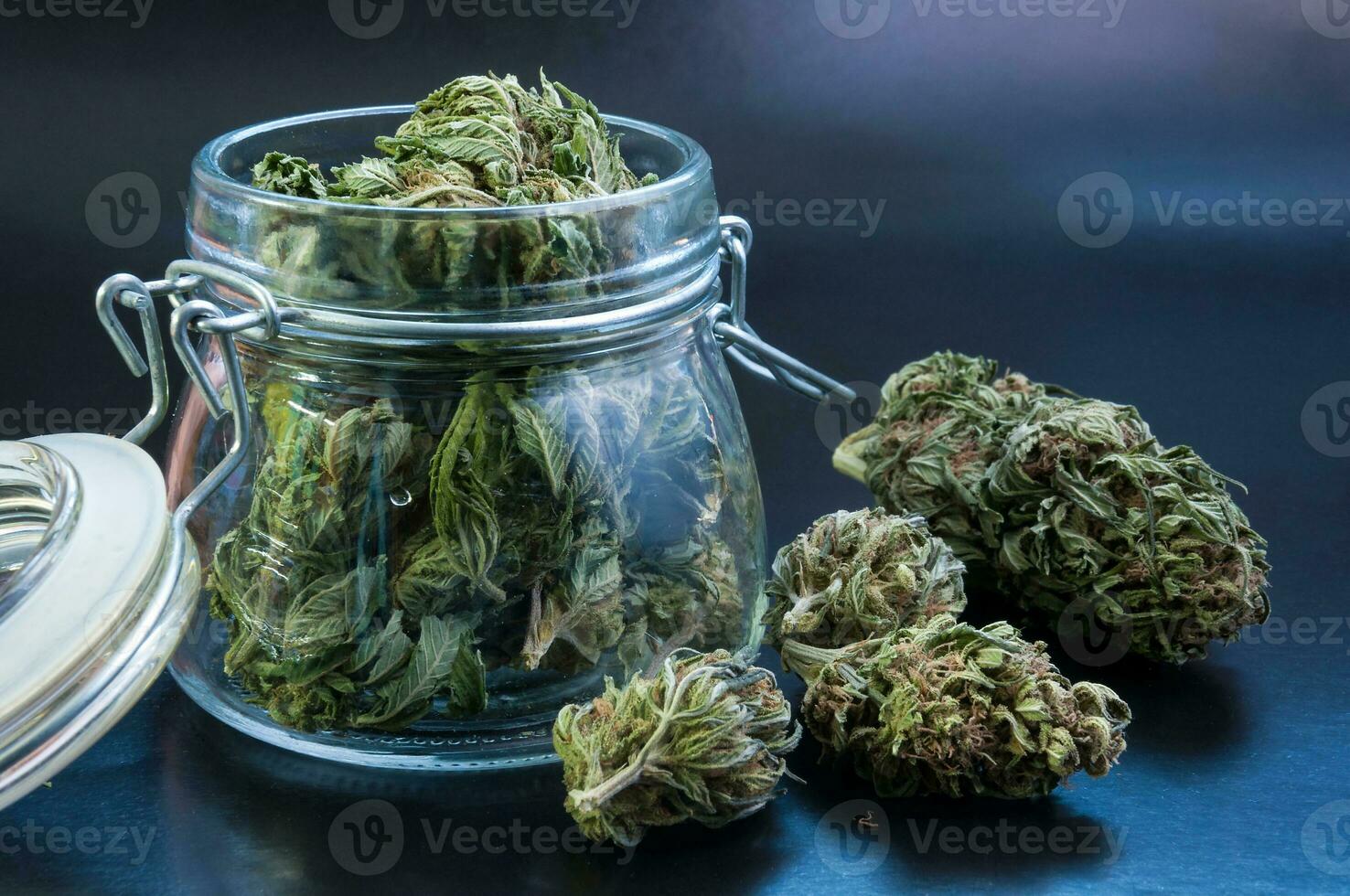 noir still life with glass mason jar full of dry medical cannabis buds on black background photo