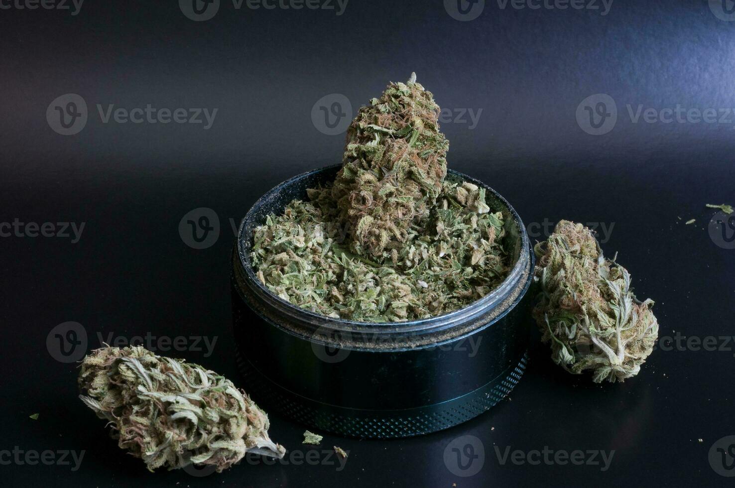 dry flowers of medical marijuana and grinder full of crushed buds close up on black background photo