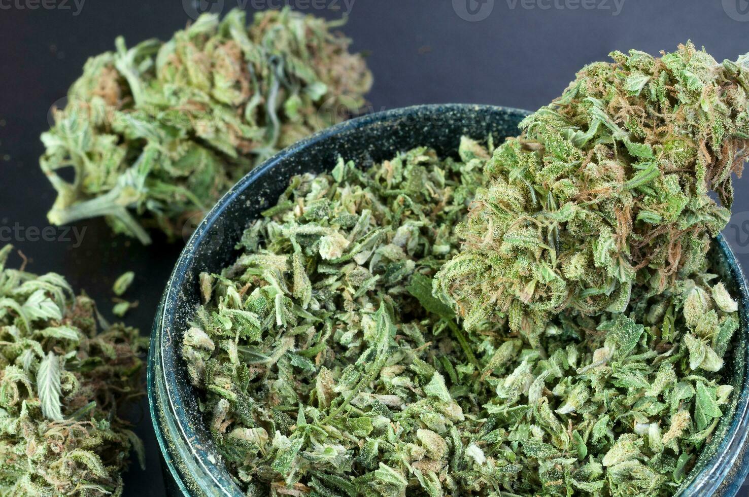 dry flowers of medical marijuana and grinder full of crushed buds close up on black background photo