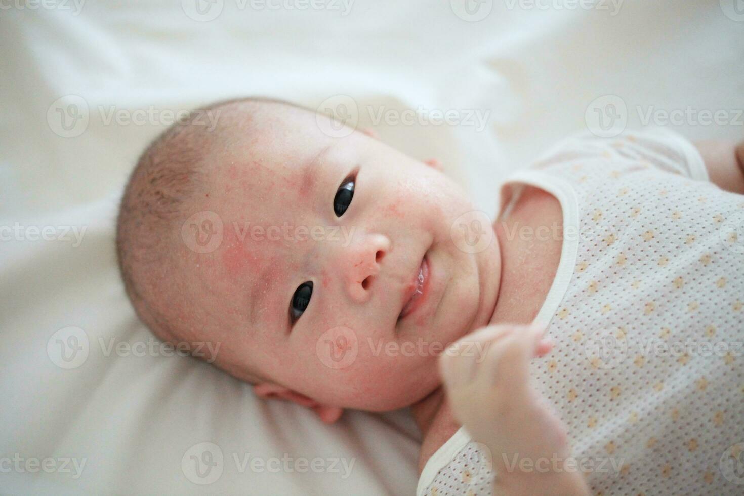 felicidad en inocencia asiático bebé chico sonrisas en acogedor cama foto