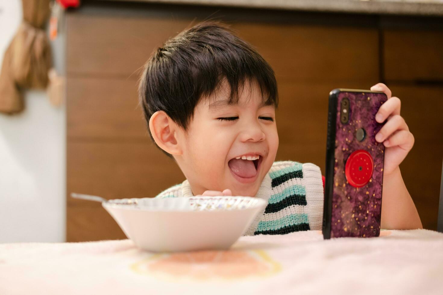 el cara de un asiático niño comiendo mientras mirando a el teléfono foto