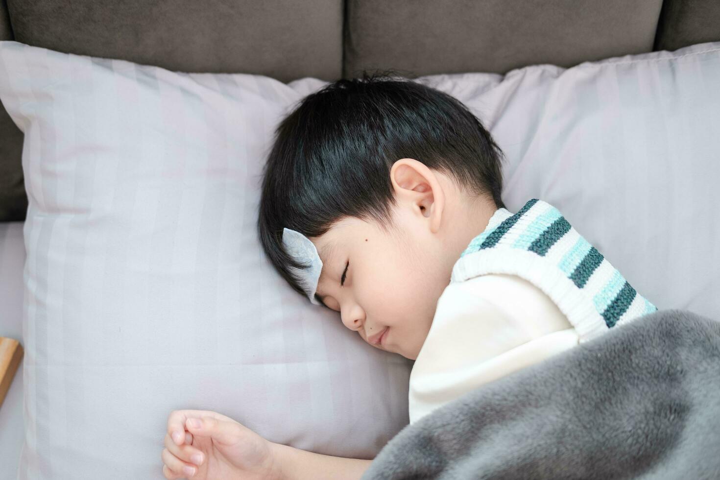 Asian boy She was sick and had a fever reducing patch on her forehead. She was lying on the bed. photo