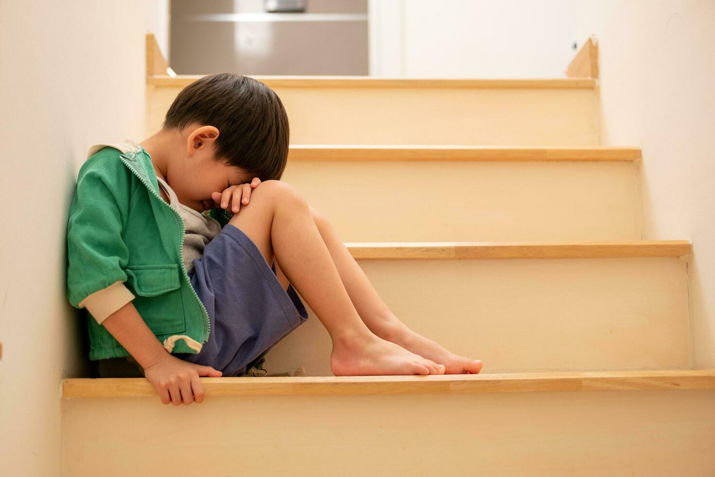 A sad Asian boy sits with his head down on the steps. photo