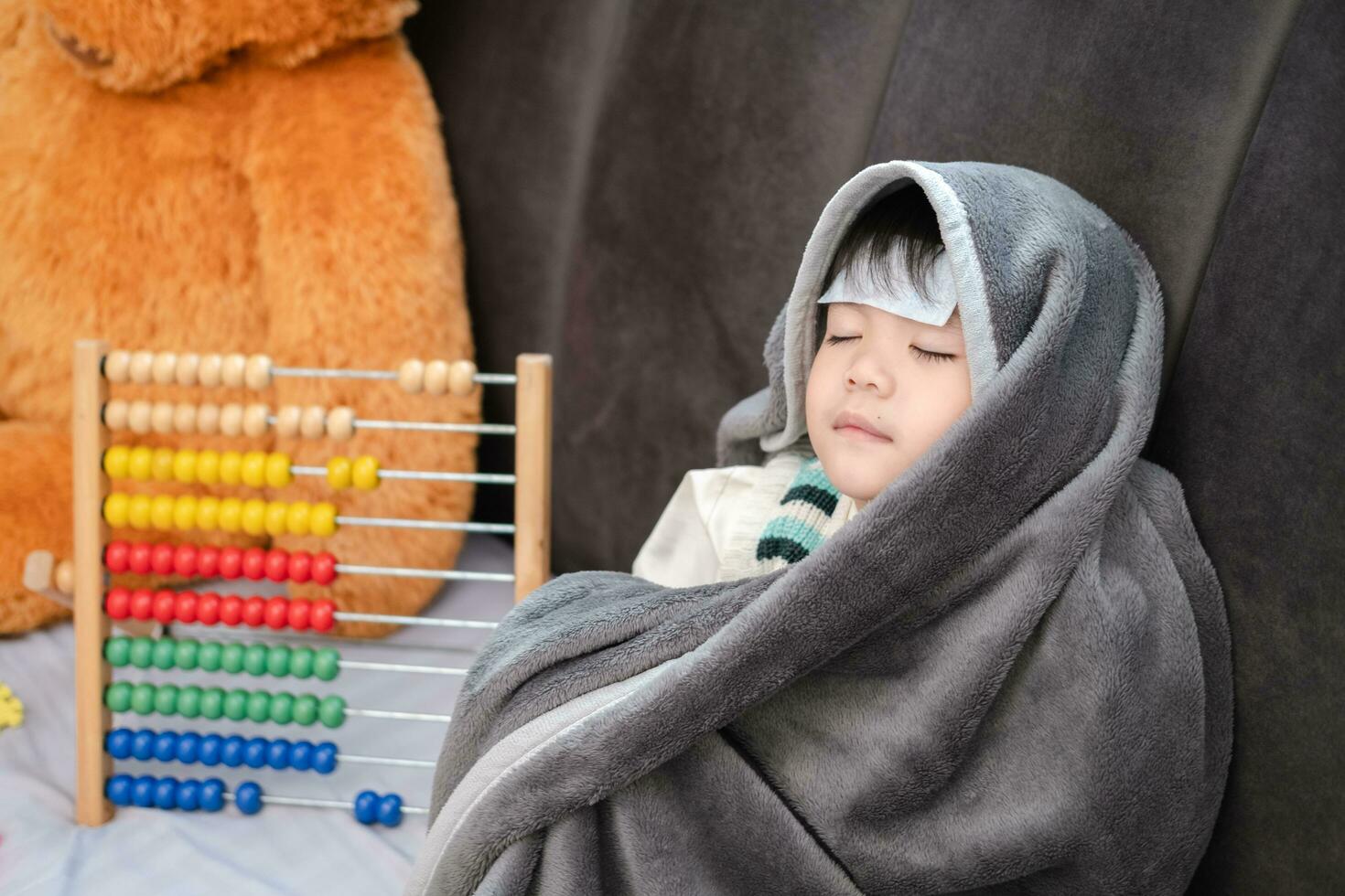 Asian boy Lying sick, he had a fever reducing patch on his forehead and covered himself with a blanket because of the cold. photo