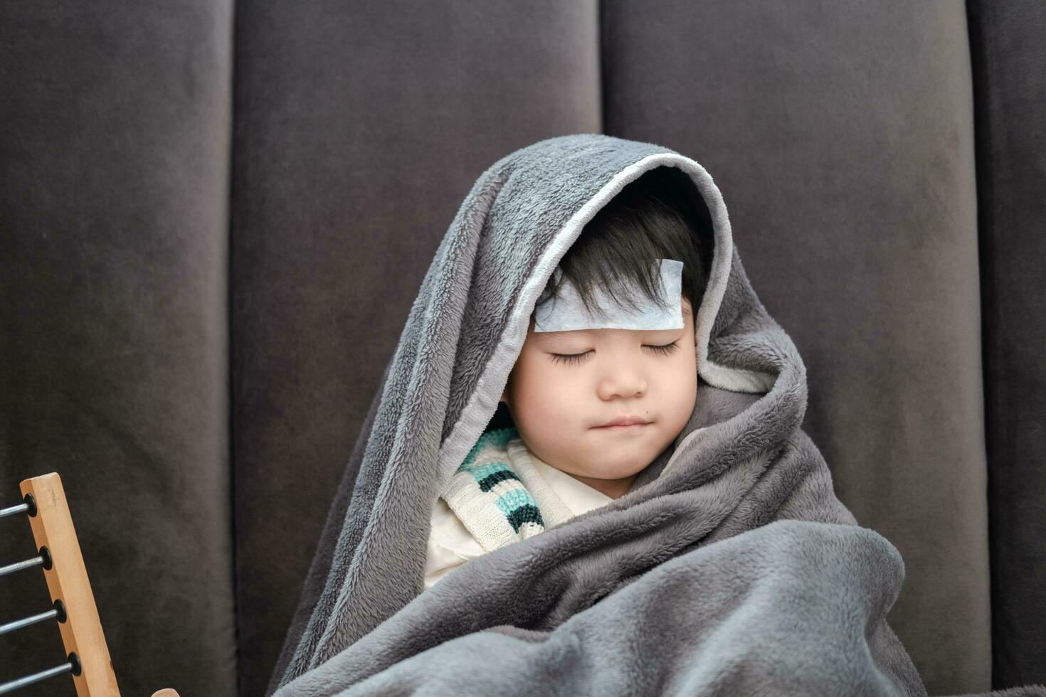 Asian boy Lying sick, he had a fever reducing patch on his forehead and covered himself with a blanket because of the cold. photo