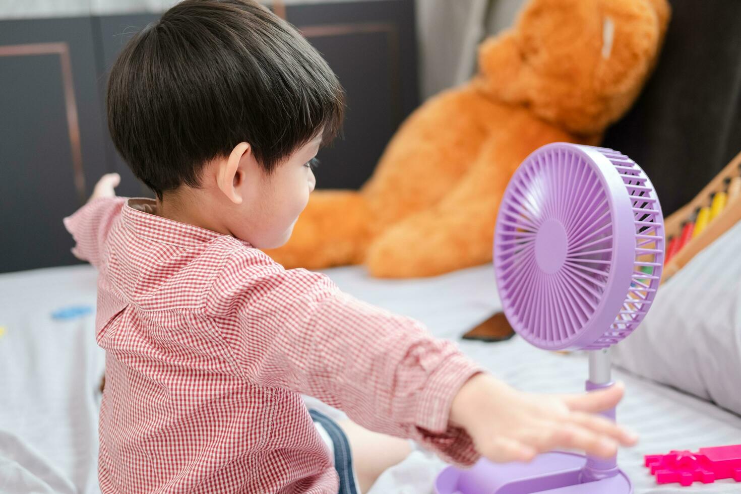 asiático chico acostado en el colchón en un caliente día jugando con un portátil ventilador felizmente foto