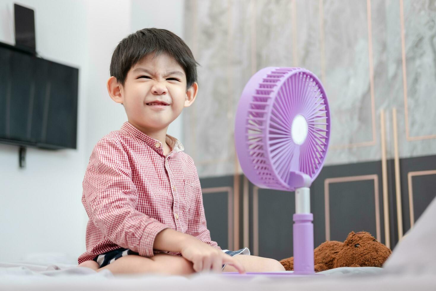 asiático chico acostado en el colchón en un caliente día jugando con un portátil ventilador felizmente foto