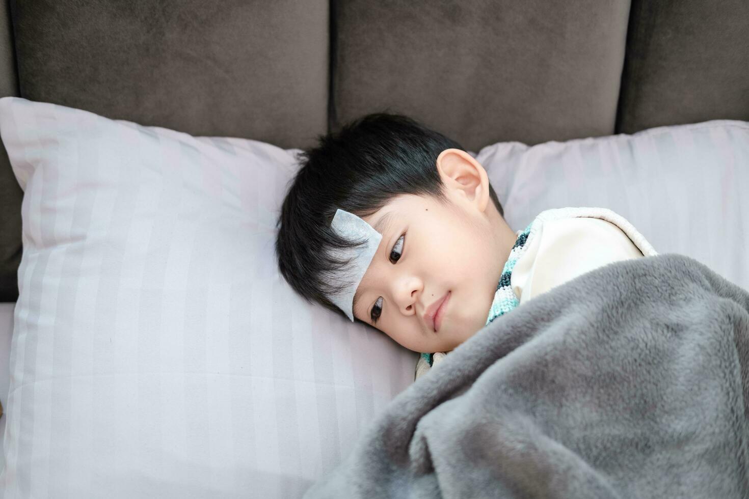 asiático chico ella estaba enfermo y tenido un fiebre reduciendo parche en su frente. ella estaba acostado en el cama. foto