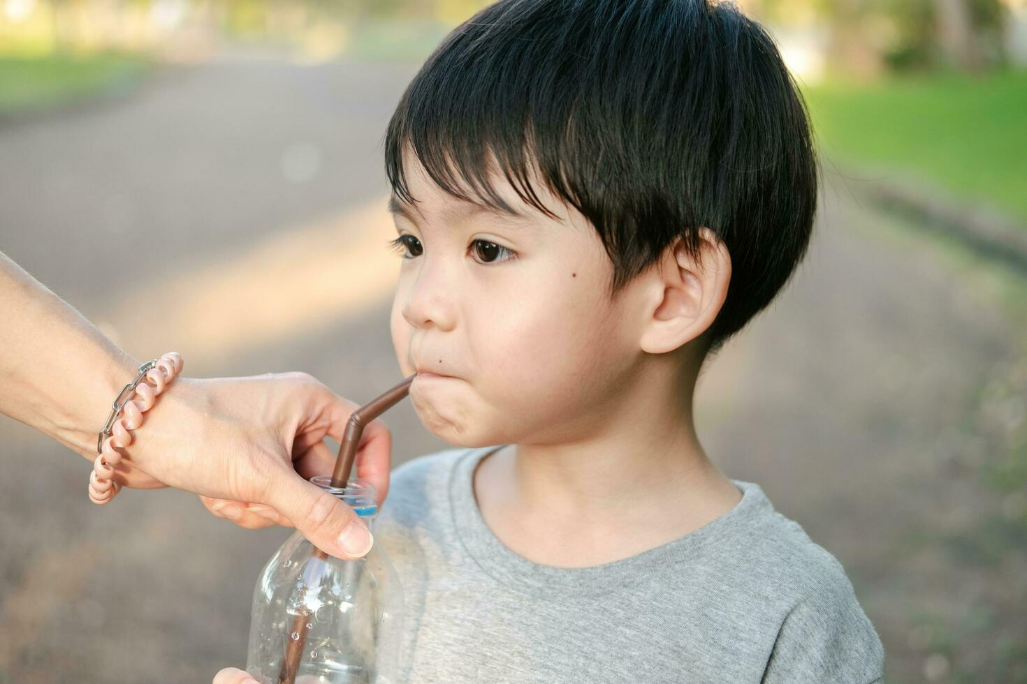 Asian boy drinking water from a bottle held by his mother photo