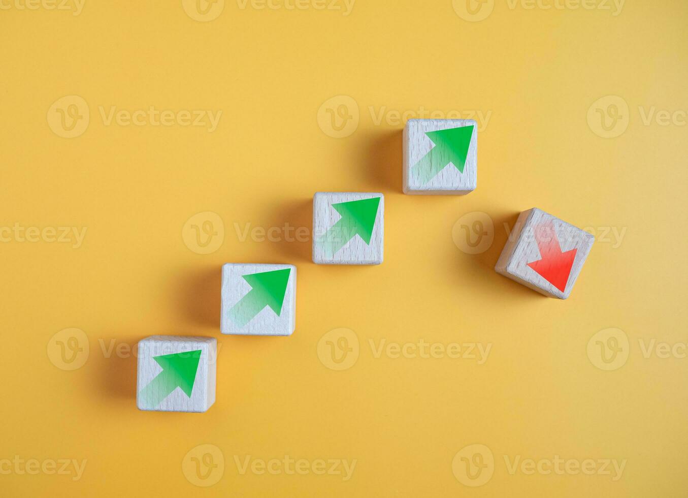 Green arrow and red arrow on wooden block represents economy trending downwards on yellow background. Economy recession crisis, inflation, stagflation, business and financial loss concept. photo