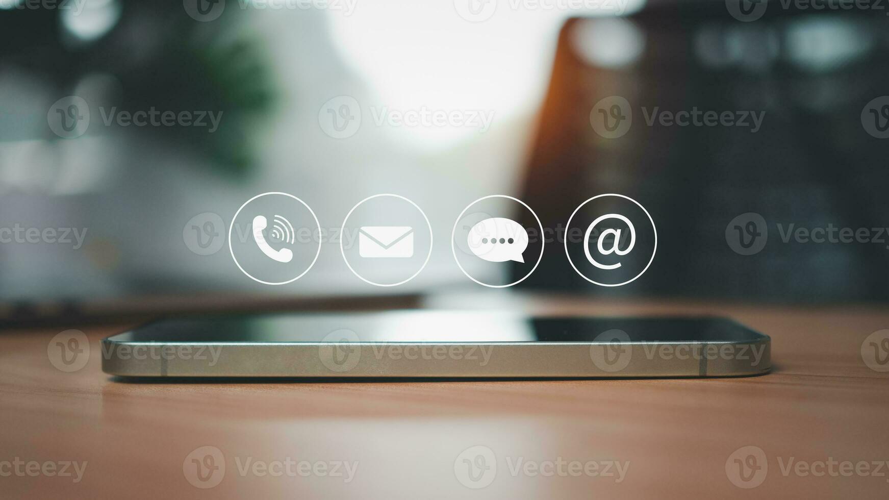 Side view of smartphone resting on wooden table surface with communication icons above representing contact us and marketing and customer support concept. photo