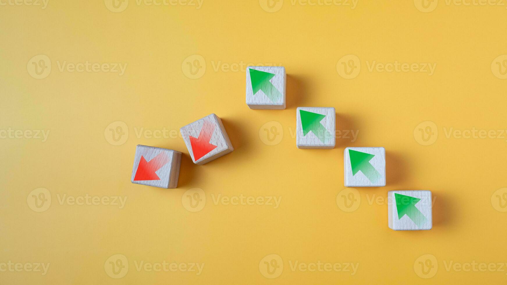 Green arrow and red arrow on wooden block represents economy trending downwards on yellow background. Economy recession crisis, inflation, stagflation, business and financial loss concept. photo