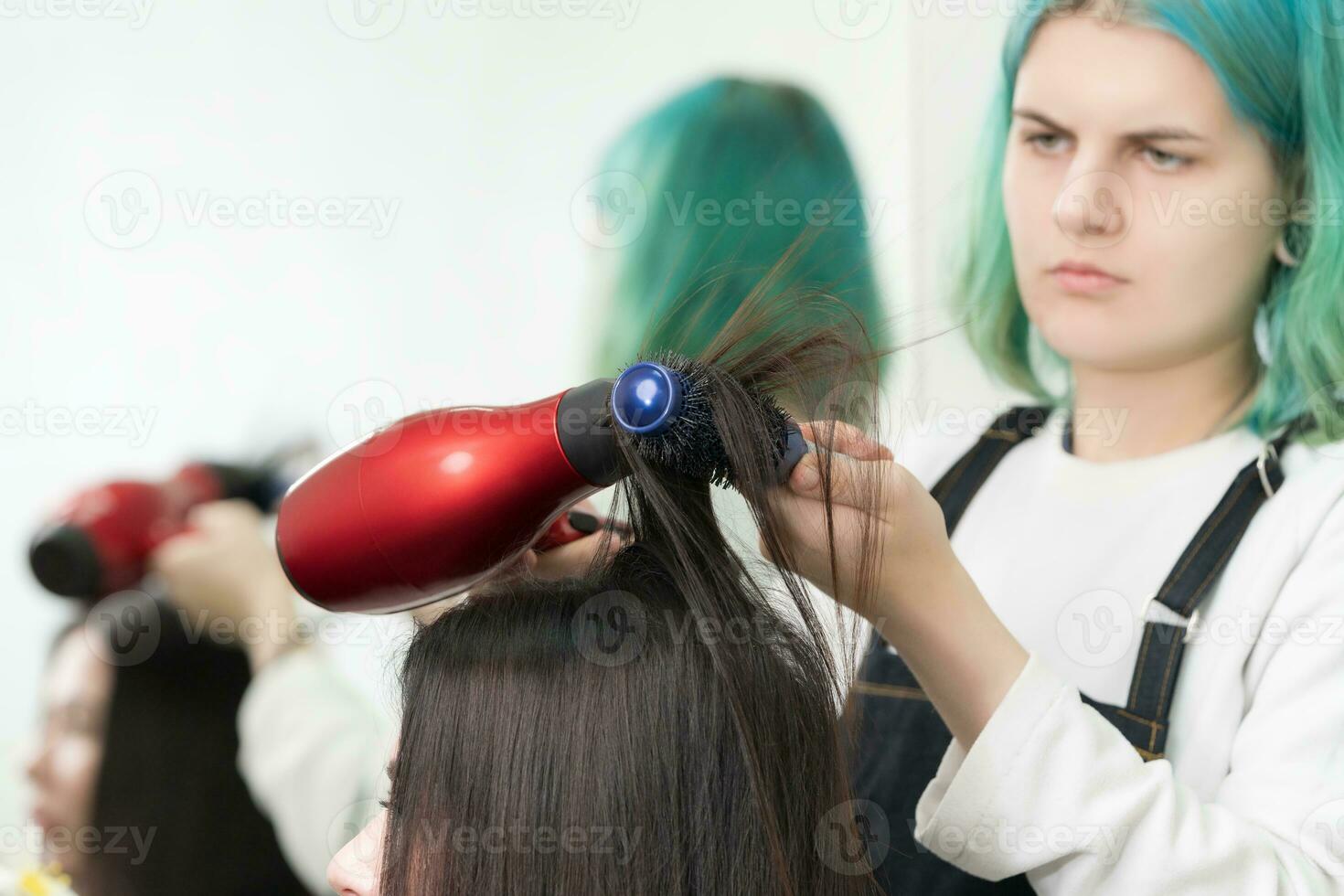 Hairstylist drying brunette hair with red hair dryer, blue hairbrush in beauty salon photo