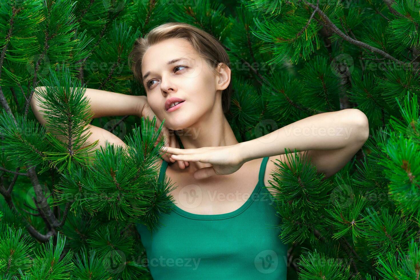 Portrait of blonde woman with short hair poses on background of evergreen shrub Dwarf Siberian Pine photo