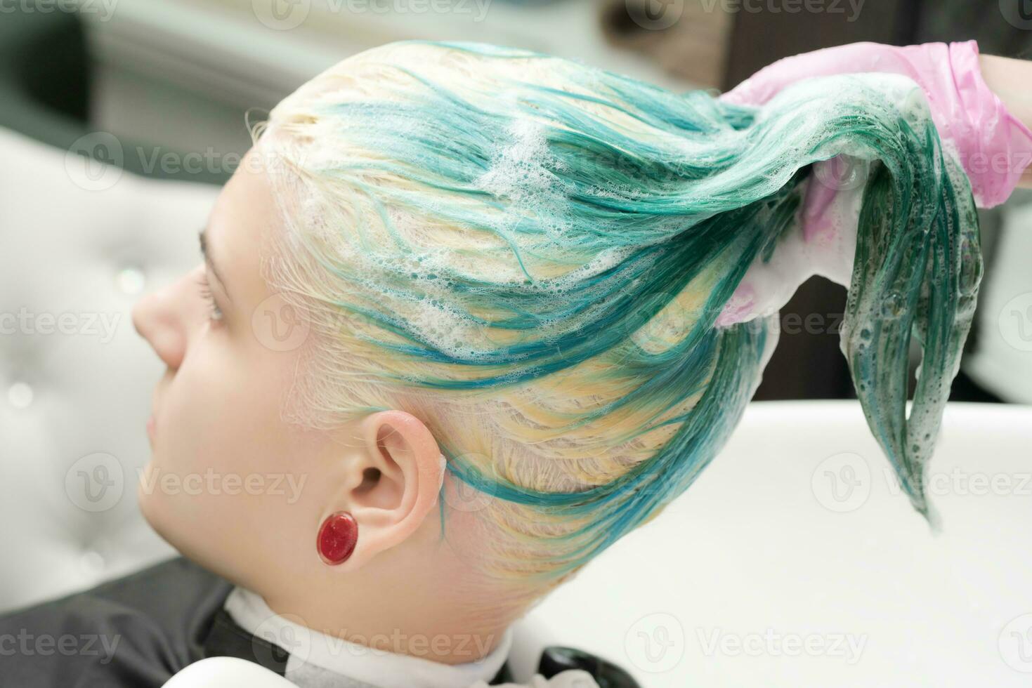 Washing emerald hair color of young woman with shampoo in beauty salon photo