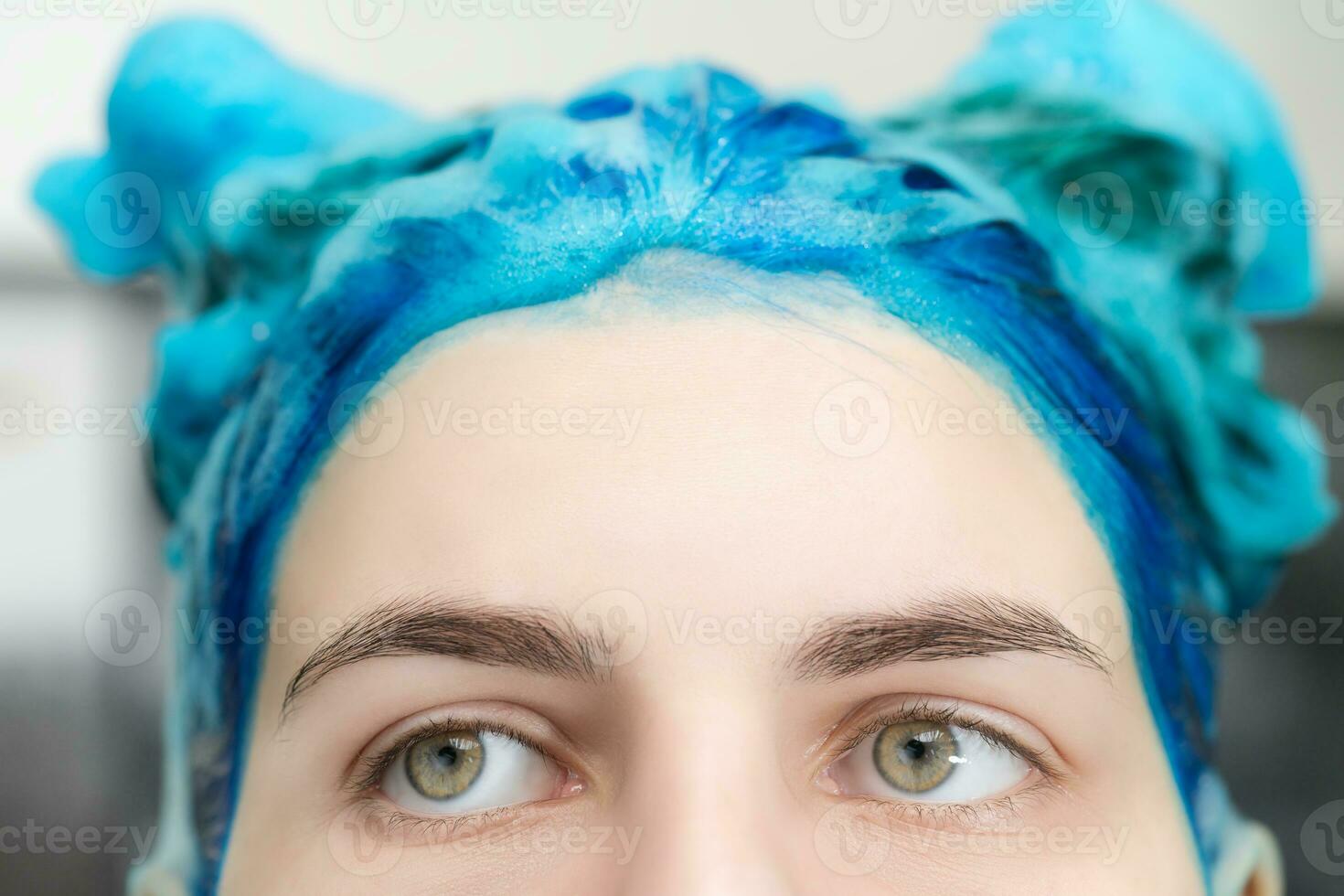 de cerca ver de niña con azul pelo y grande ojos con champú aplicado mientras Lavado su pelo después tintura su zafiro pelo en belleza salón foto